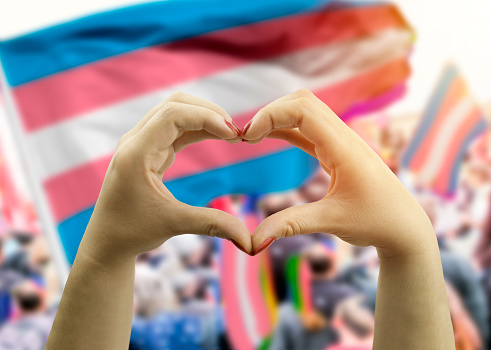 close up hands creating a heart with  transgender flag in the background