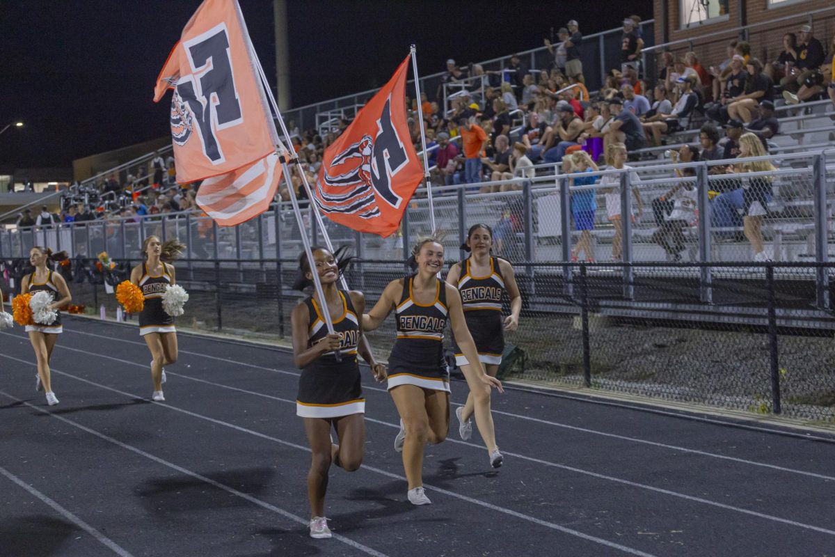 Cheerleaders Ava Medlin, Maddie Hunt, Emma Baker and Abi Brockway running down the track at a football game.